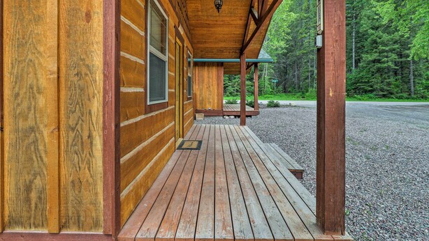 A wooden cabin with a porch, a wooden deck, and a view of a forested area. - Hungry Horse Cabin: Deck, Fire Pit, Near Glacier! (Hungry Horse)