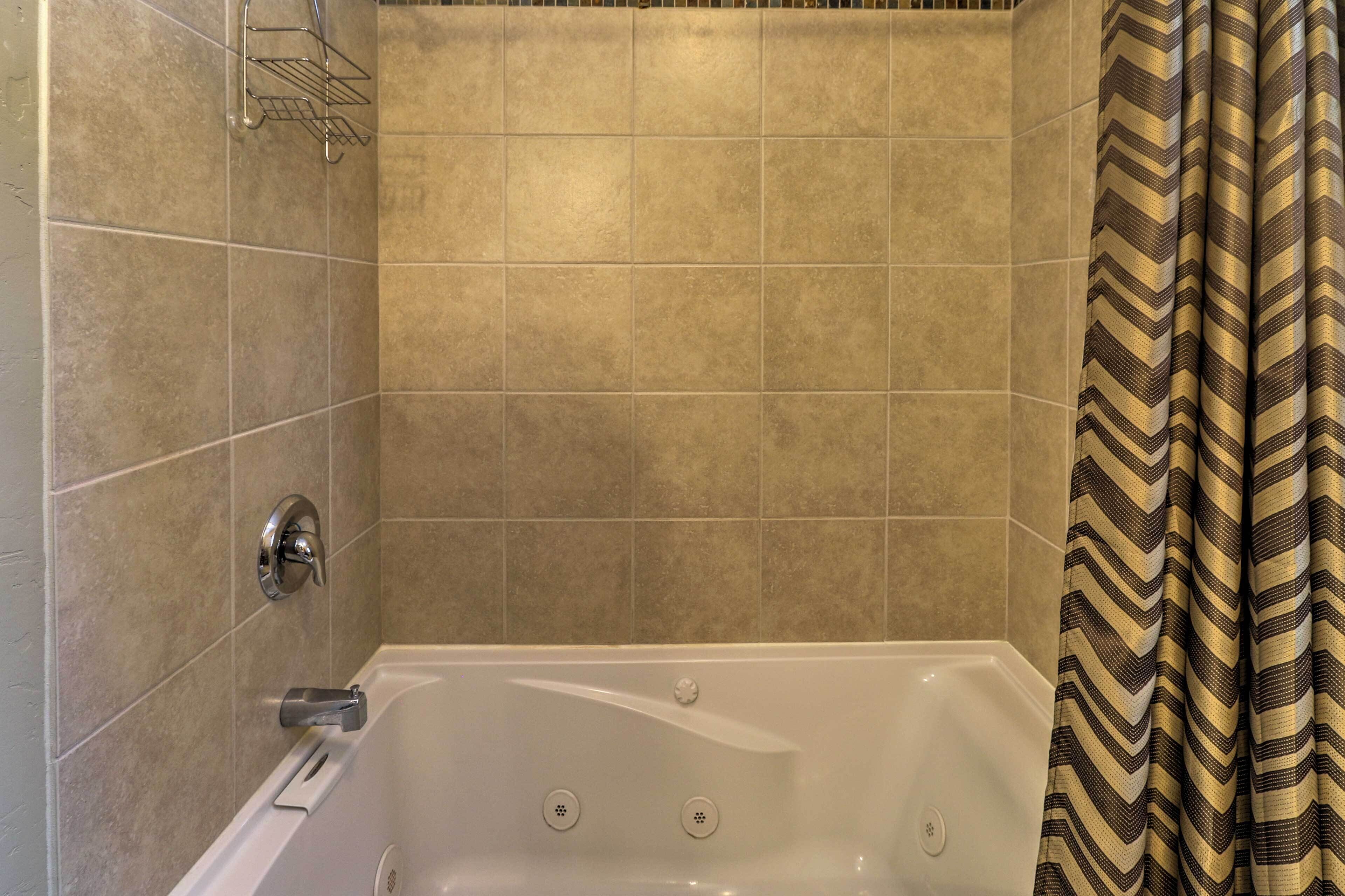 Un baño con bañera, paredes de azulejos, cortina de ducha y toallero.
