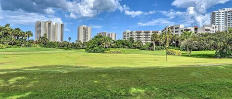 A well-maintained grassy area with a clear sky and tall buildings in the background.