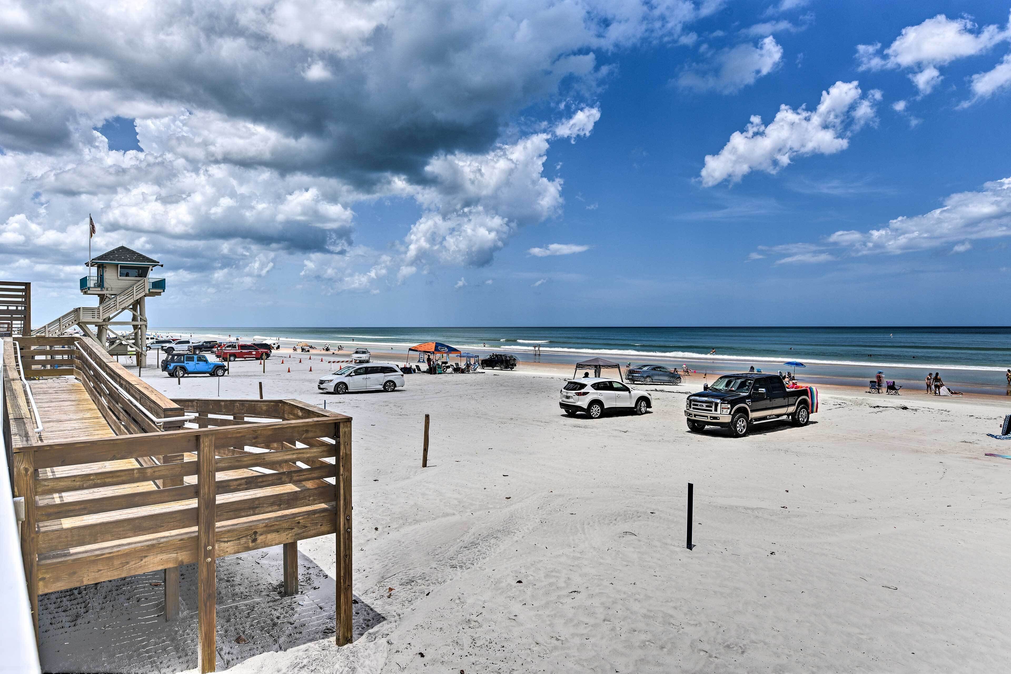 A beach with a lifeguard tower, wooden deck, and several parked cars.