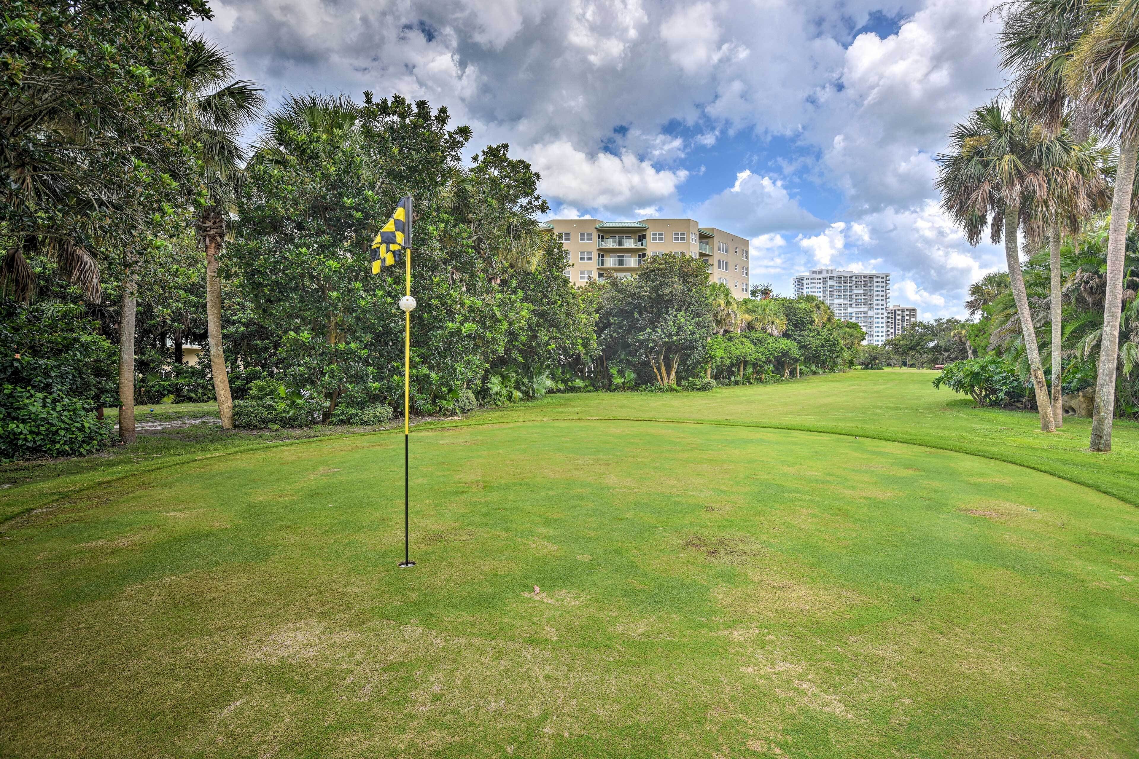 A golf course with a flagstick, surrounded by lush greenery and palm trees.
