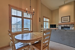 A dining area with a wooden table and chairs, large windows, a stone fireplace, and a television. - Keystone Ski Condo w/ Mtn View - Walk to Gondola! (Keystone)