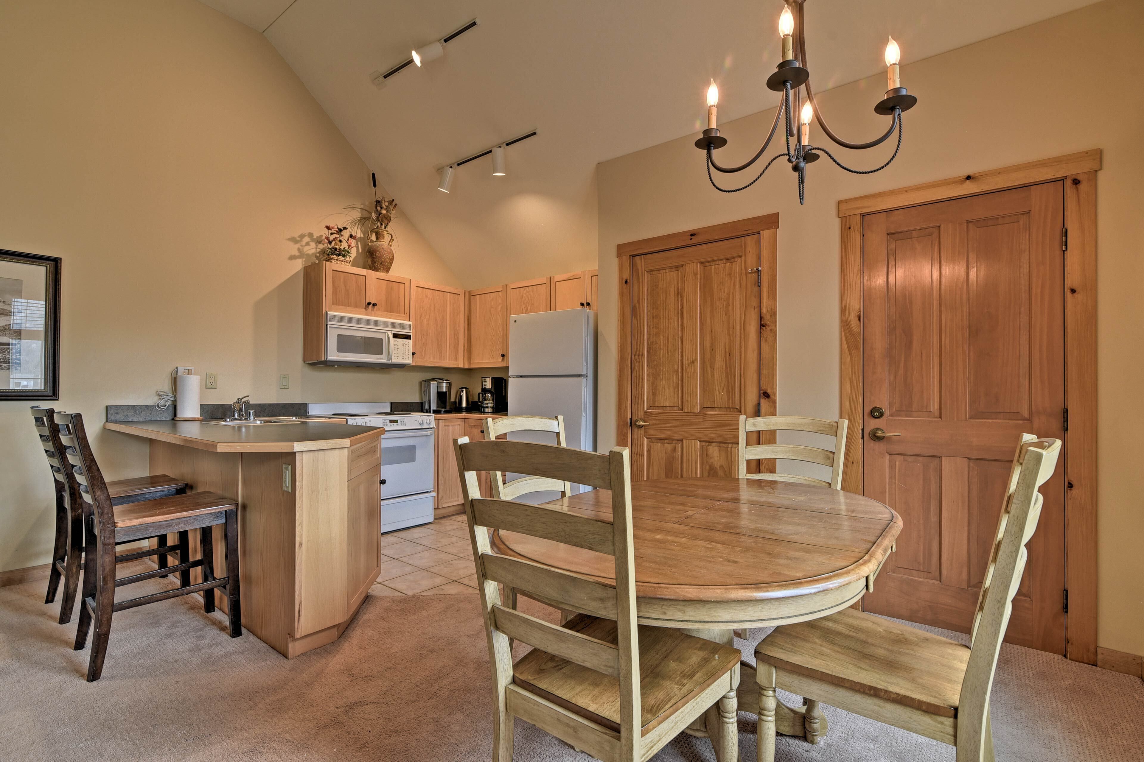 A kitchen with wooden cabinets, a central island with bar stools, a dining table with chairs, a chandelier, and a wooden door.