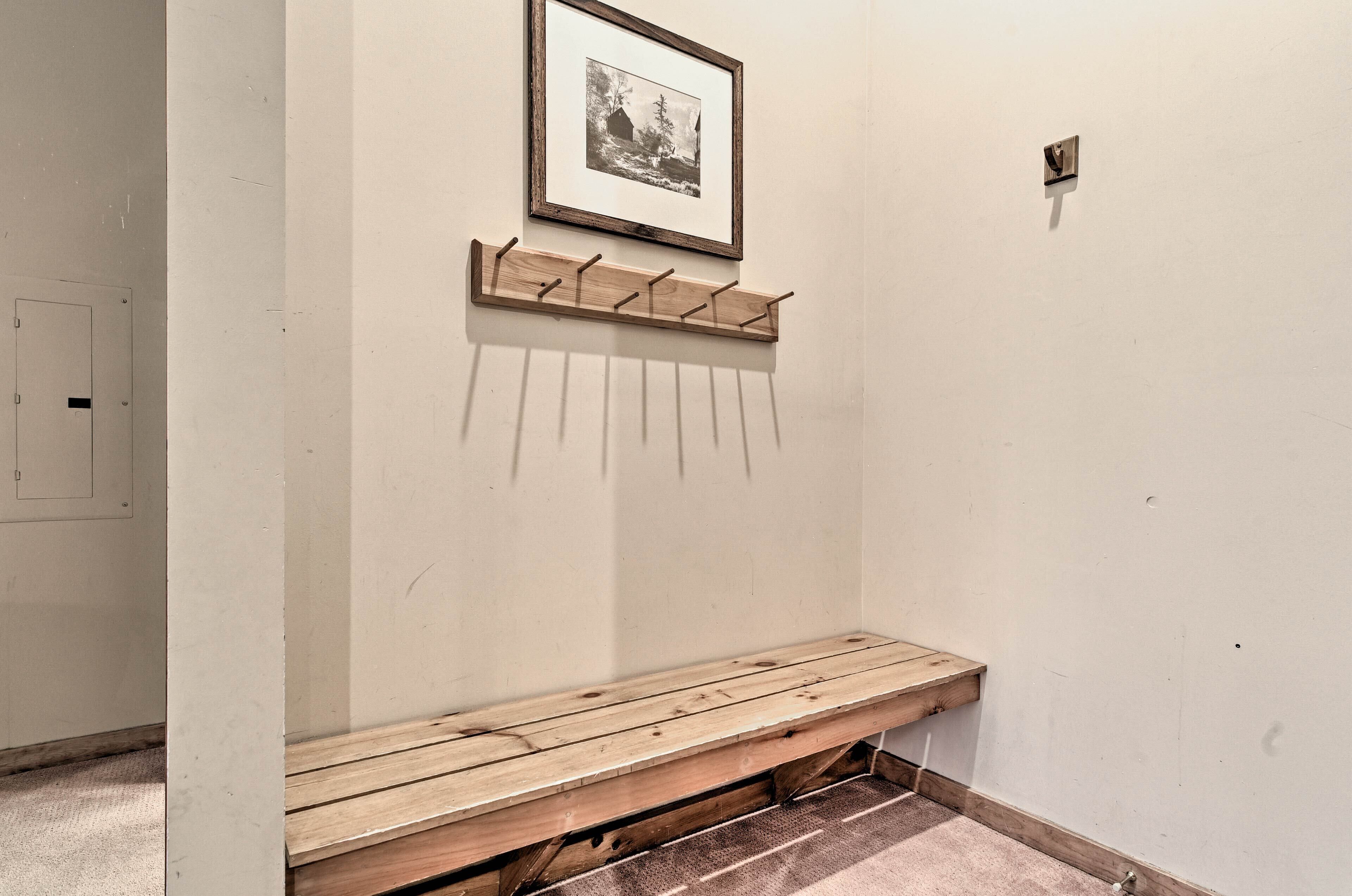 A hallway with a wooden bench, a coat rack, and a framed picture on the wall.
