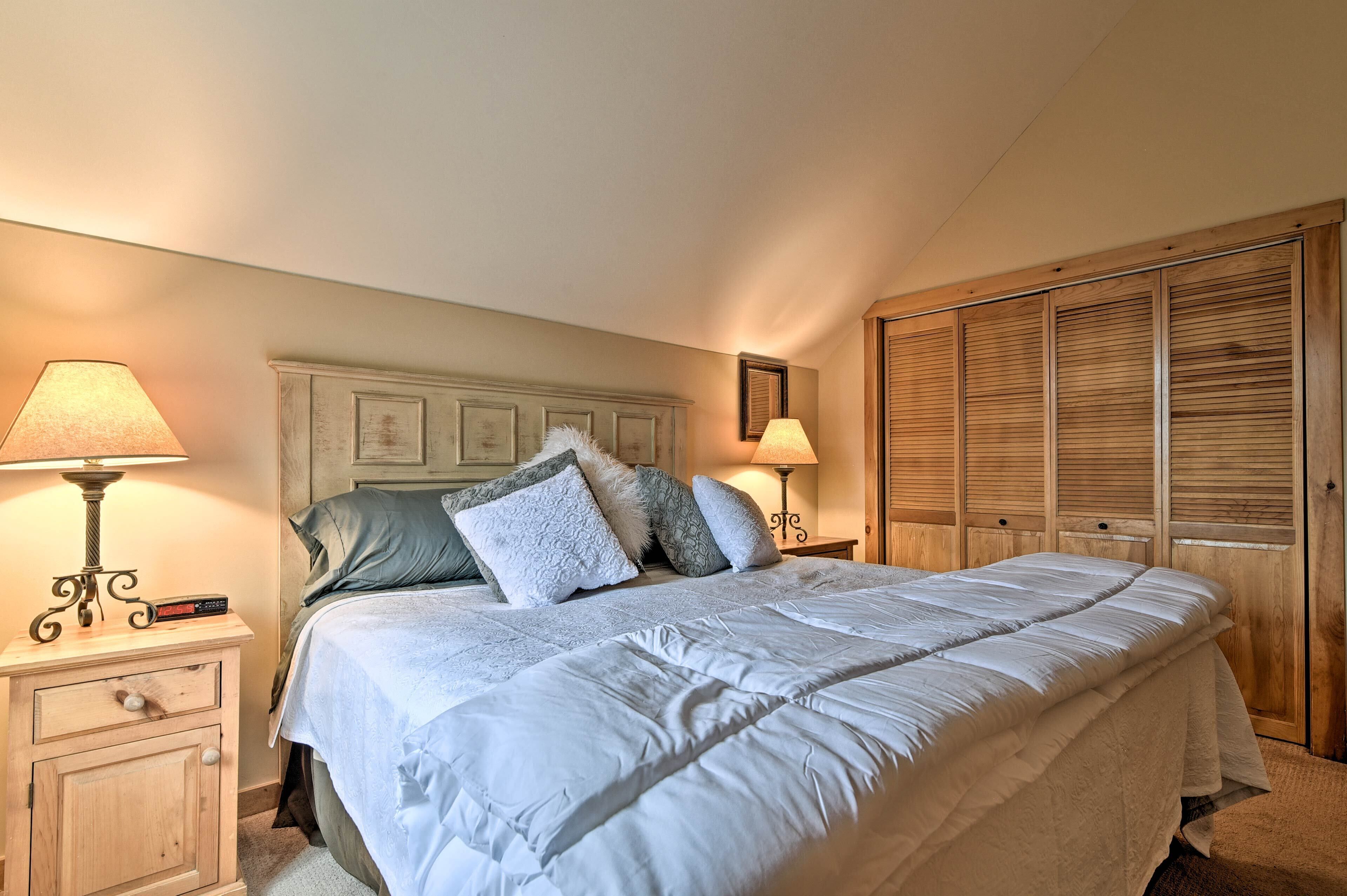 Une chambre à coucher avec un grand lit, une tête de lit en bois, deux tables de chevet avec des lampes, une armoire et un tableau encadré au mur.