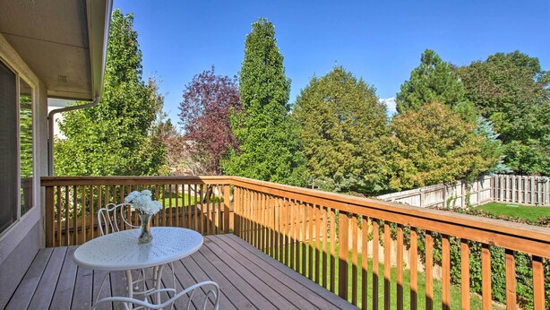 A wooden deck with a round table and chairs, a white railing, and a view of a fenced yard with trees.