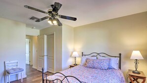 A bedroom with a bed, two bedside lamps, a ceiling fan, a chair, and a door leading to another room.