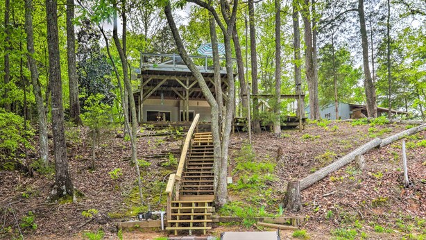 Un escalier en bois mène à un chalet situé dans une zone boisée, avec des murs en pierre et une terrasse en bois.