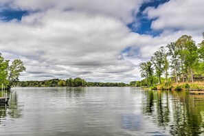 Un lago tranquilo con un muelle, rodeado de árboles y un cielo nublado.