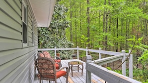Une terrasse en bois, agrémentée de chaises en osier et d’une petite table, le tout entouré d’une végétation luxuriante.