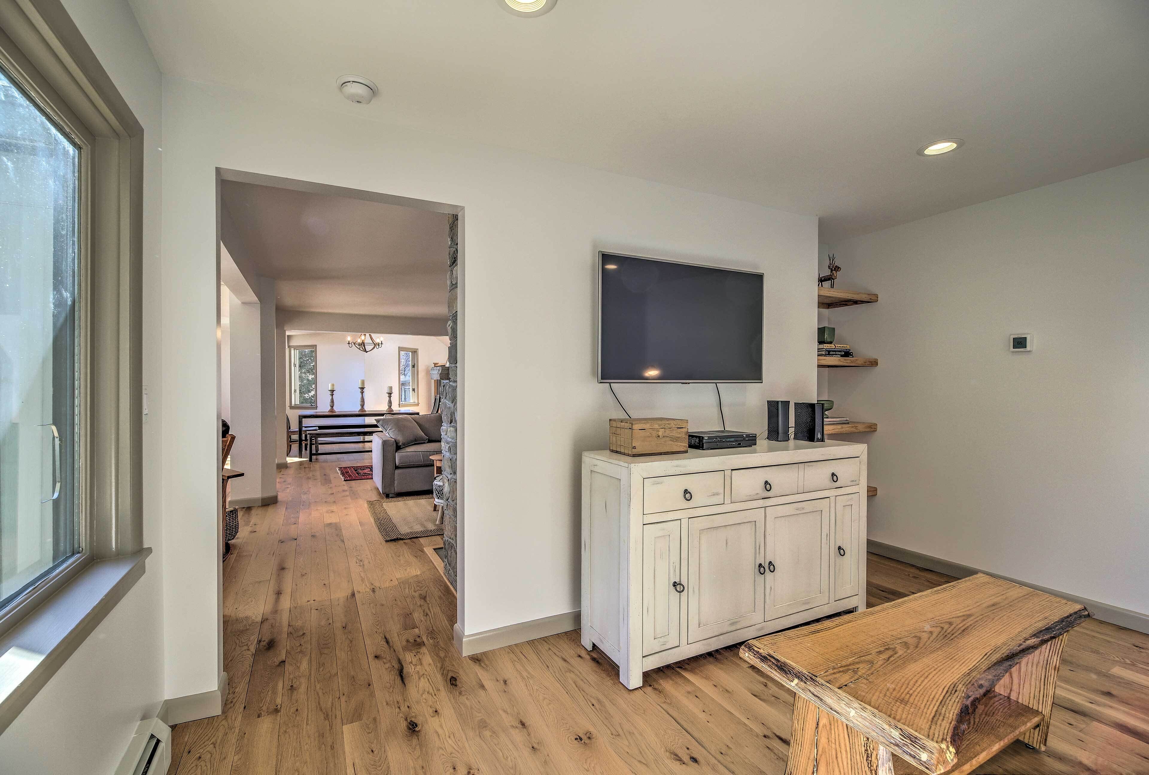 A spacious living room with a wooden floor, a white cabinet with a flat-screen TV, and a dining area with a wooden table.