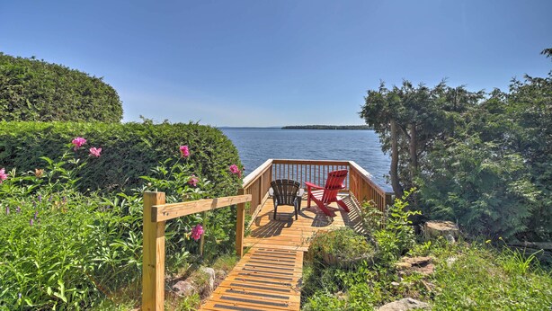 A wooden deck with two chairs overlooking a body of water, surrounded by lush greenery. - Plattsburgh Home w/ Deck on Lake Champlain (Plattsburgh)