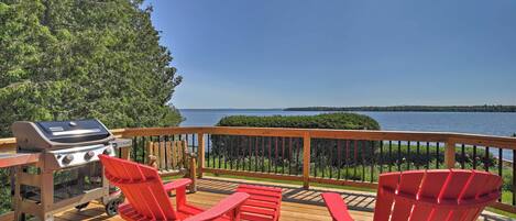 Une terrasse avec un barbecue, des chaises Adirondack rouges et une vue sur un lac.