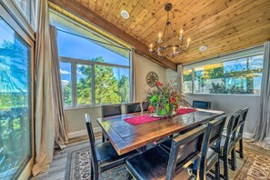 A dining area with a wooden table, black chairs, a chandelier, and large windows with curtains.