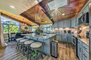 A spacious kitchen with granite countertops, a central island with stools, and a large window overlooking greenery. - Serene Alto Cabin w/ Mountain Views & Fire Pit! (Alto)