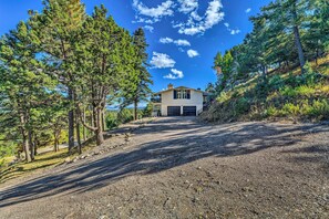 A house with a gravel driveway, surrounded by tall pine trees.