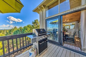 A balcony with a grill, a dining area, and a view of trees.