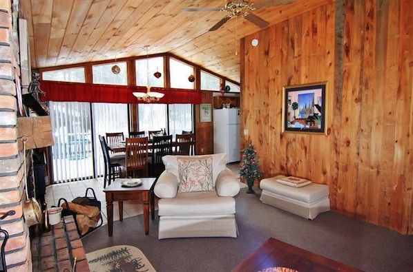Una sala de estar acogedora con chimenea, paredes de madera, un comedor y un pequeño árbol de Navidad.