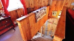 A wooden staircase with a patterned rug, a wooden desk, and a chair in a room with wooden walls and a window with red curtains. - South Londonderry Home, Walk to Magic Mtn Ski Area (Londonderry)
