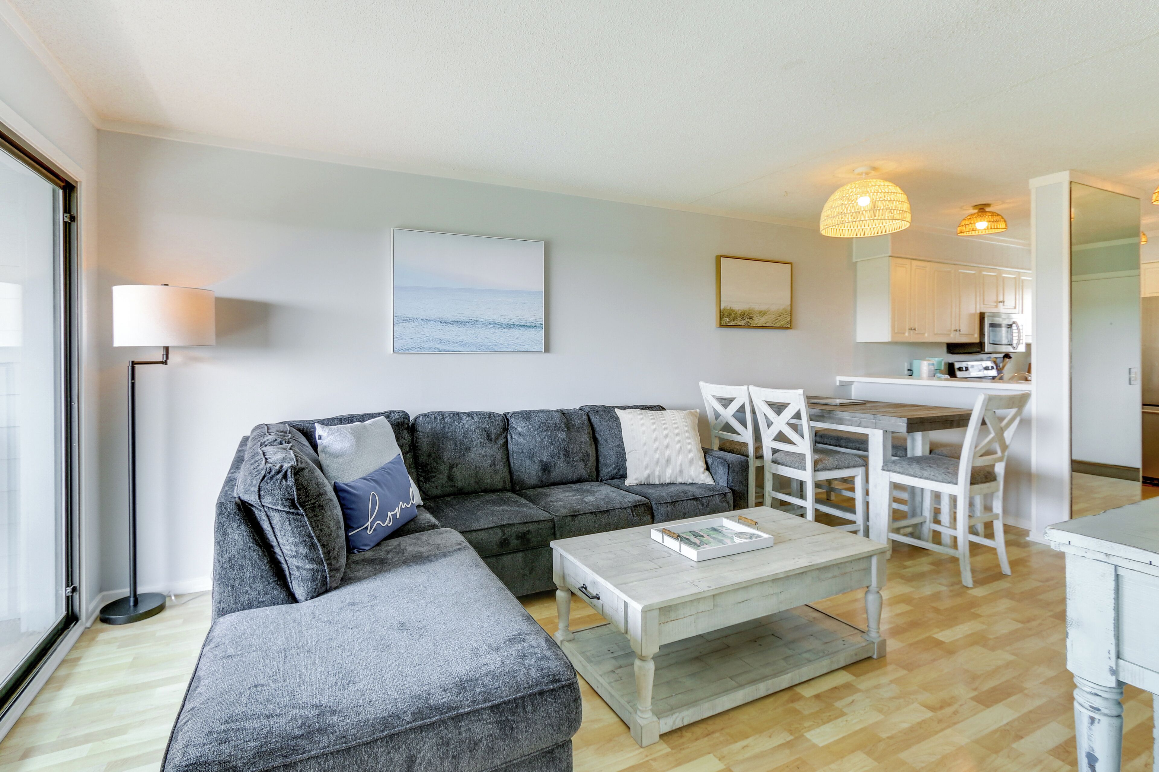 A modern living room with a grey sectional sofa, a wooden coffee table, and a dining area with white chairs.