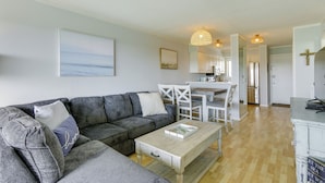 Een moderne woonkamer met een grijze modulaire bank, een houten salontafel en een eethoek met witte stoelen en een tafel.