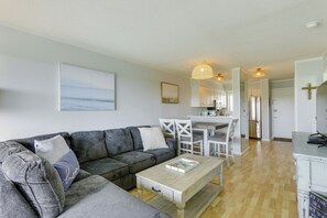 A modern living room with a grey sectional sofa, a wooden coffee table, and a dining area with white chairs and a table. - Beautiful Views, Walk to Beach: Hilton Head Condo (Hilton Head Island)