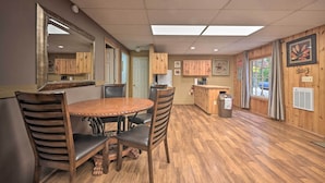 Un coin repas avec une table et des chaises en bois, un espace cuisine avec des placards en bois et un grand miroir au mur.