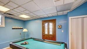 Une table de billard avec des billes, un panneau d’accueil, une porte avec des panneaux de verre et une lampe.