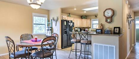 A kitchen with a dining area, wooden cabinets, a refrigerator, a clock, and a chandelier.