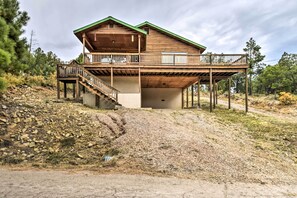 A two-story wooden cabin with a balcony on the upper floor, situated on a hillside with a gravel driveway. - Ruidoso Home w/ Deck & Grill, Near Grindstone Lake (Ruidoso)