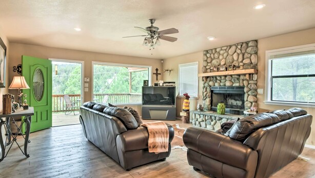 A spacious living room with two leather sofas, a fireplace, a television, and a stone wall. - Ruidoso Home w/ Deck & Grill, Near Grindstone Lake (Ruidoso)