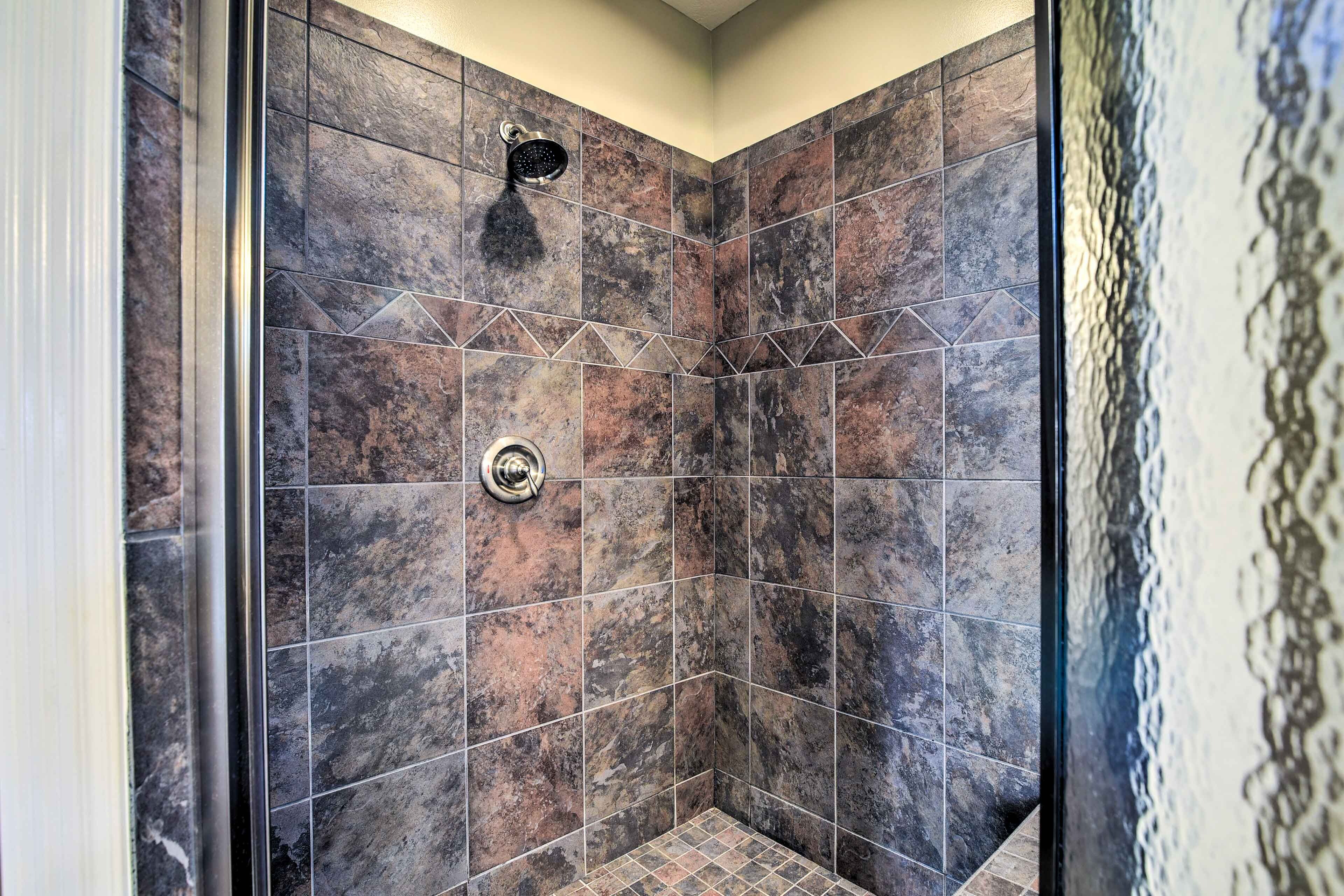 A shower with dark, textured tiles and a visible showerhead.