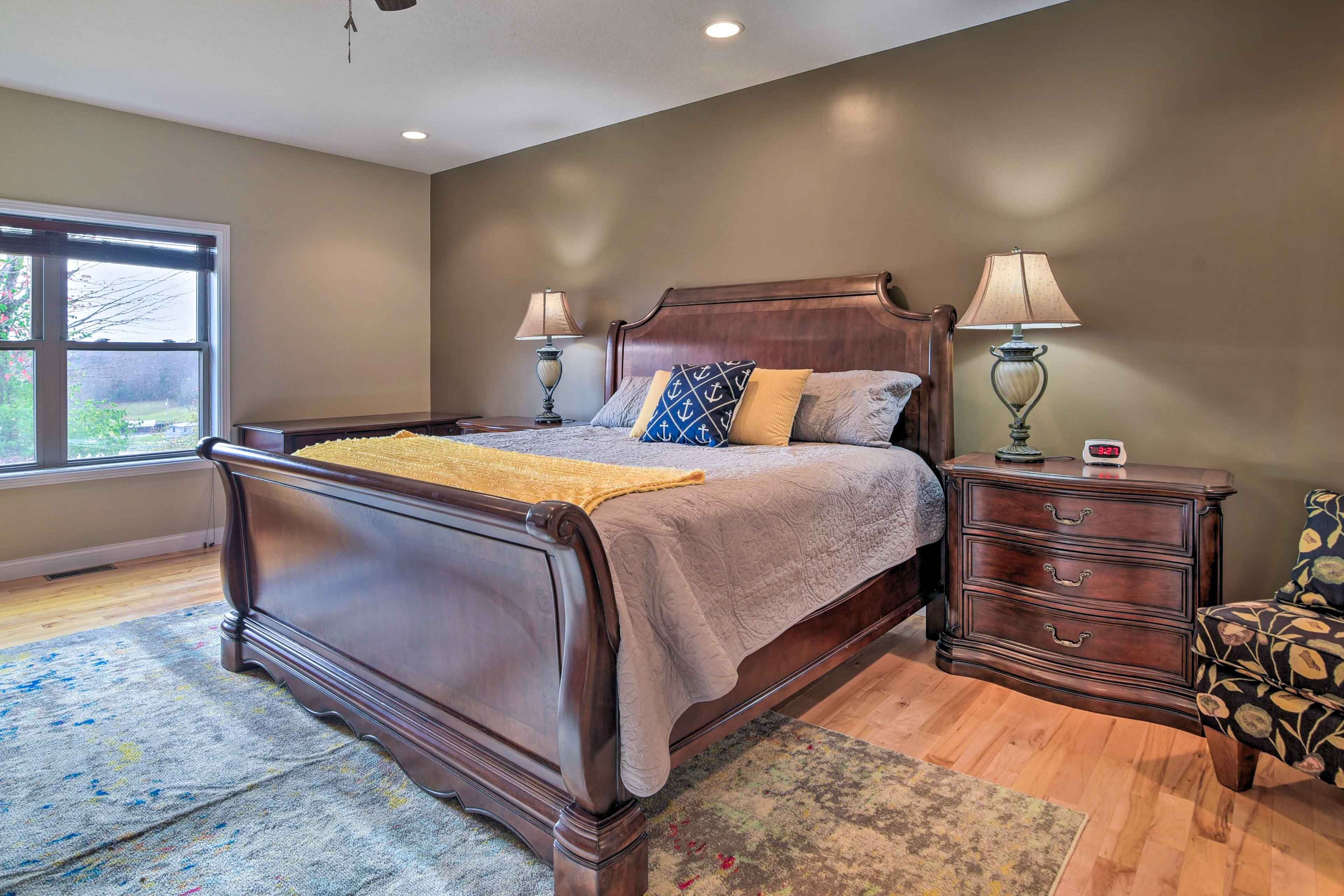 A bedroom with a large bed, two bedside tables, a nightstand, and a window with a view.