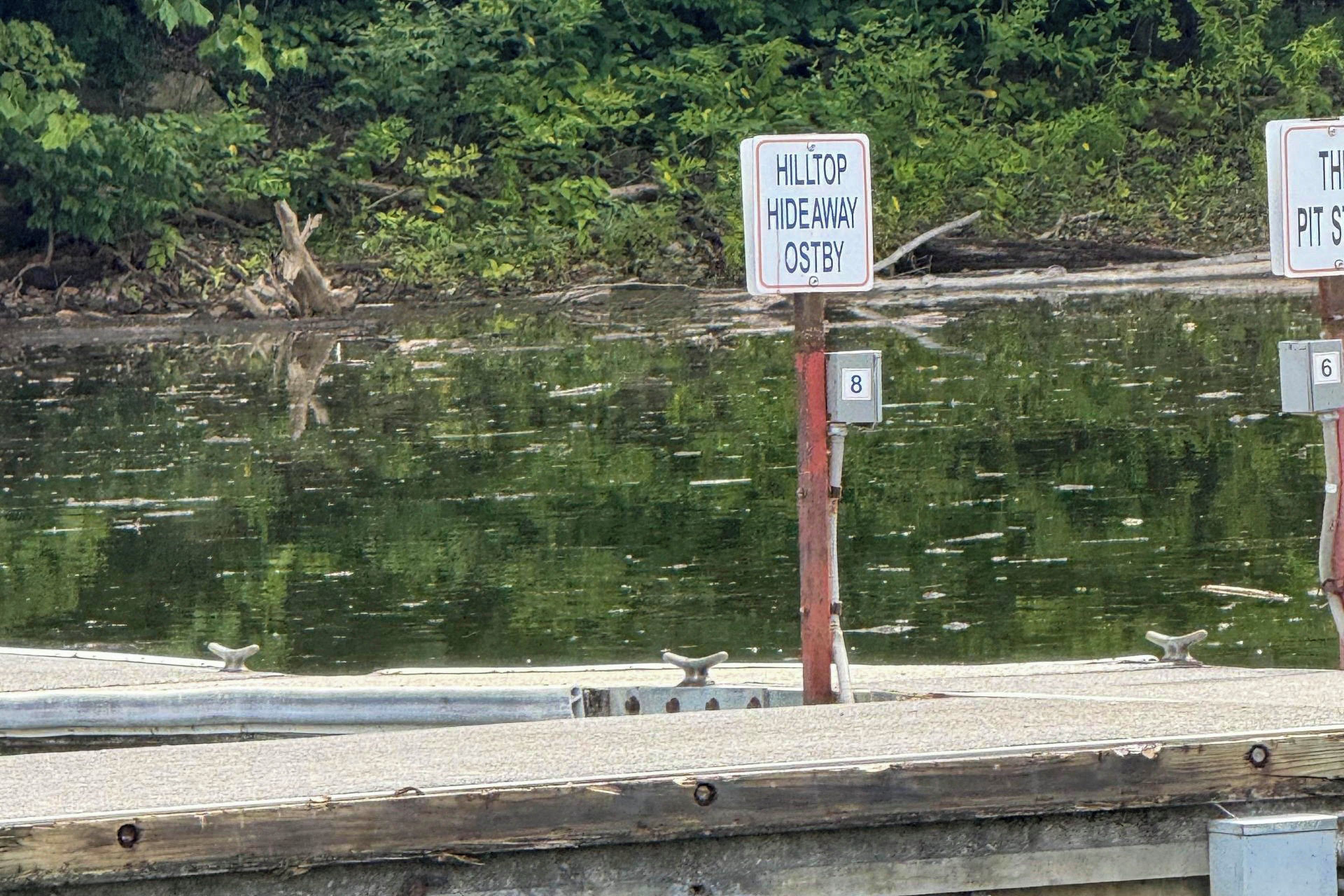 A signpost with 'HILTOP HIDEAWAY OSTBY' and a number '6' on a wooden post near a body of water.