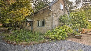 Une maison en pierre avec une allée gravillonnée, entourée d’une végétation luxuriante et d’un petit jardin.