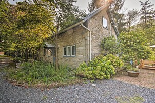 Una casa de piedra con camino de grava, rodeada de abundante vegetación y un pequeño jardín.