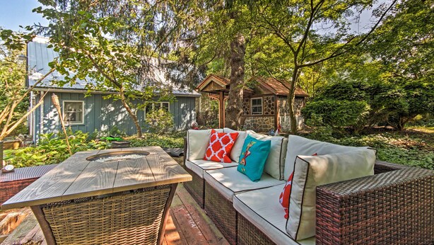 Un espace extérieur accueillant, aménagé avec une table en osier et des canapés confortables, le tout entouré d’une végétation luxuriante et d’arbres.