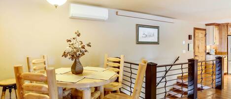 A dining area with a round table, wooden chairs, a vase with dried flowers, and a staircase with a metal railing.