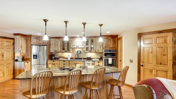 A kitchen with wooden cabinets, a stainless steel refrigerator, a built-in oven, and a large island with bar stools. - Modern Deadwood Apt With Mountain Views & Grill! (Lead)