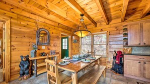 Interior de una cabaña de madera con una mesa de comedor, bancos, una araña y una estatua de oso.