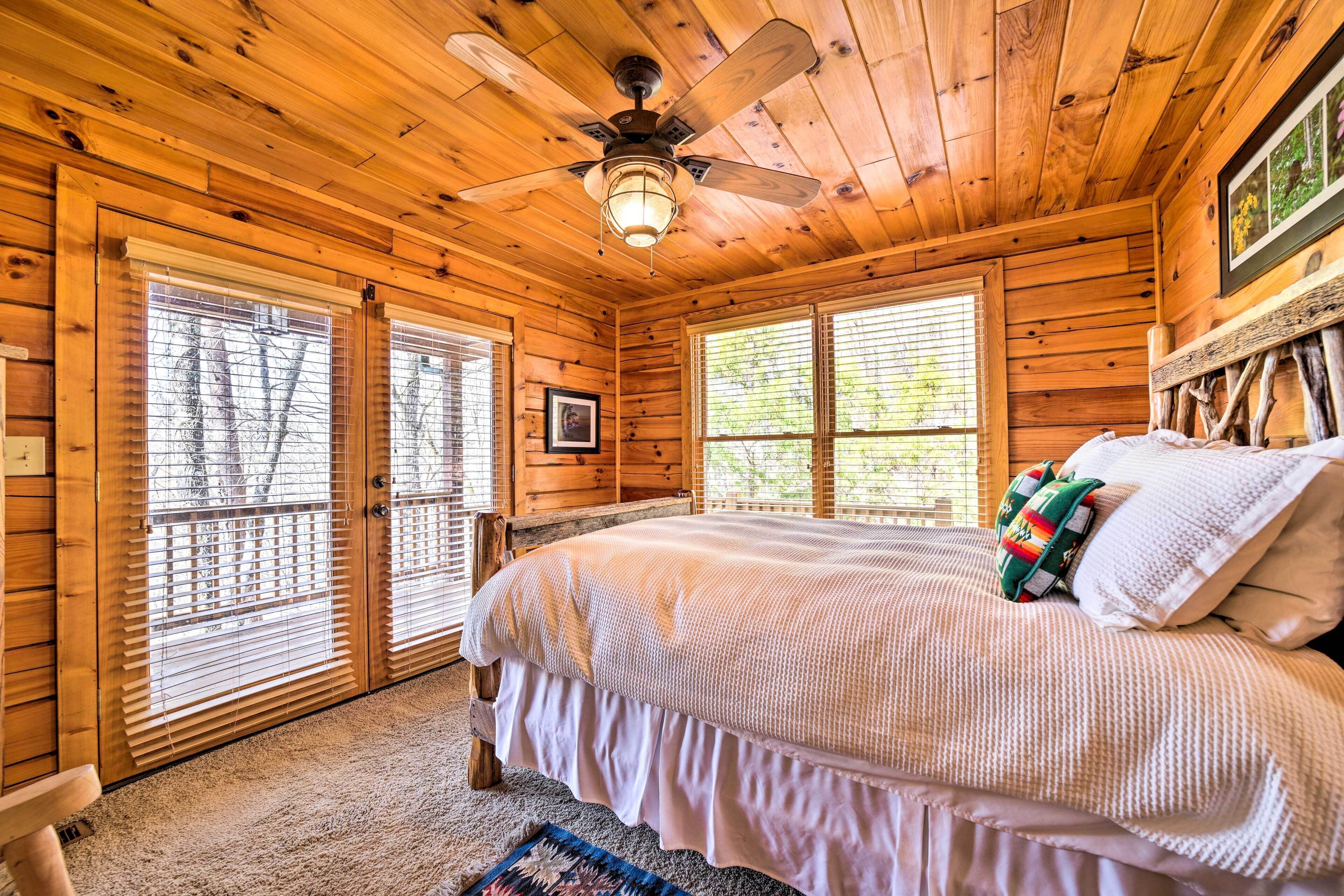 A wooden cabin bedroom with a bed, a ceiling fan, and large windows.