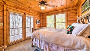 Un dormitorio de cabaña de madera con una cama, un ventilador de techo y ventanas grandes.