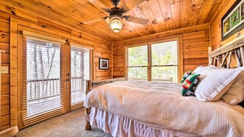 A wooden cabin bedroom with a bed, a ceiling fan, and large windows.