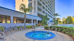 Ein Hotelpool mit Liegestühlen, einem Whirlpool und einem Gebäude mit Balkonen im Hintergrund.
