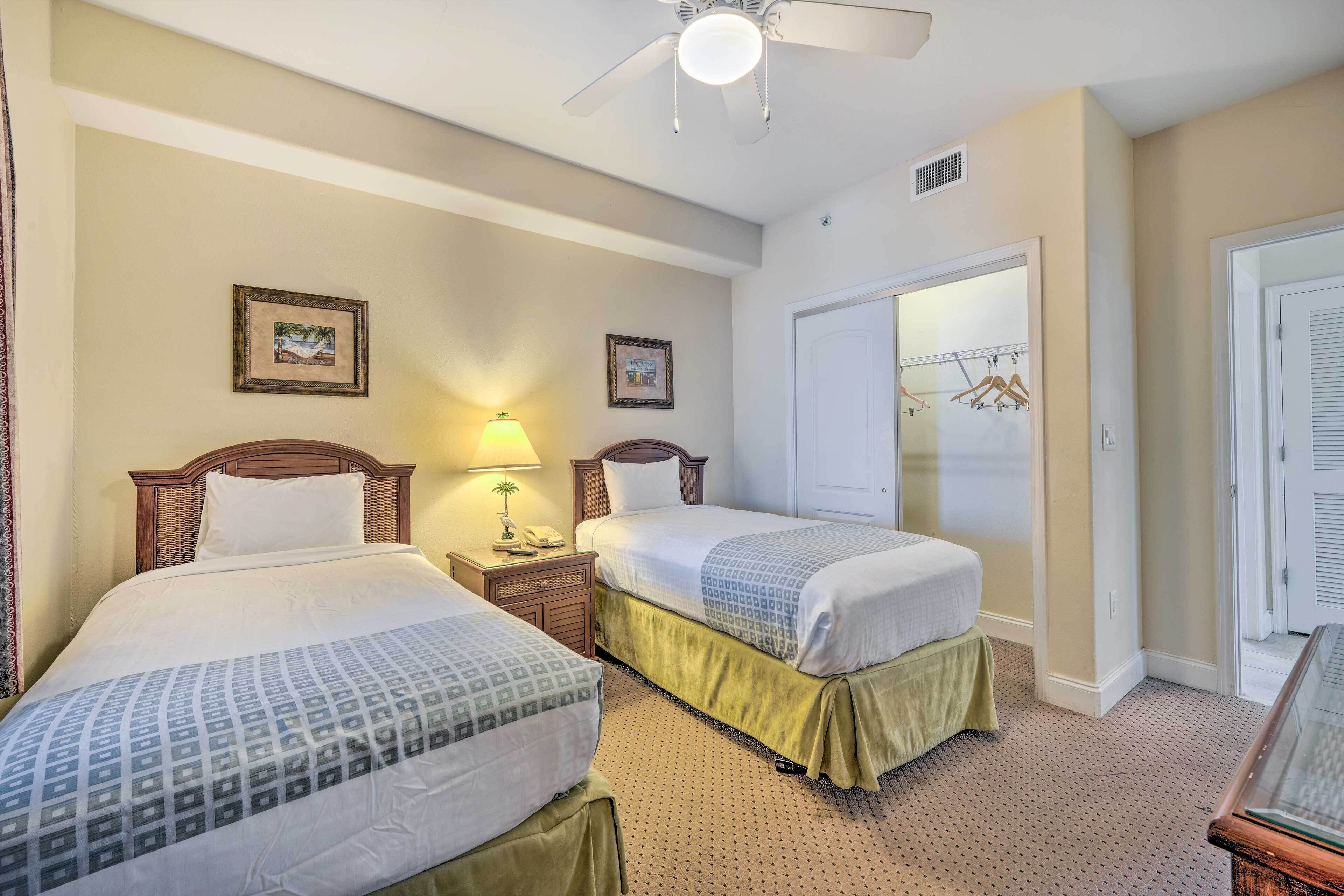 A hotel room with two beds, a ceiling fan, a nightstand with a lamp, and a door leading to a closet.