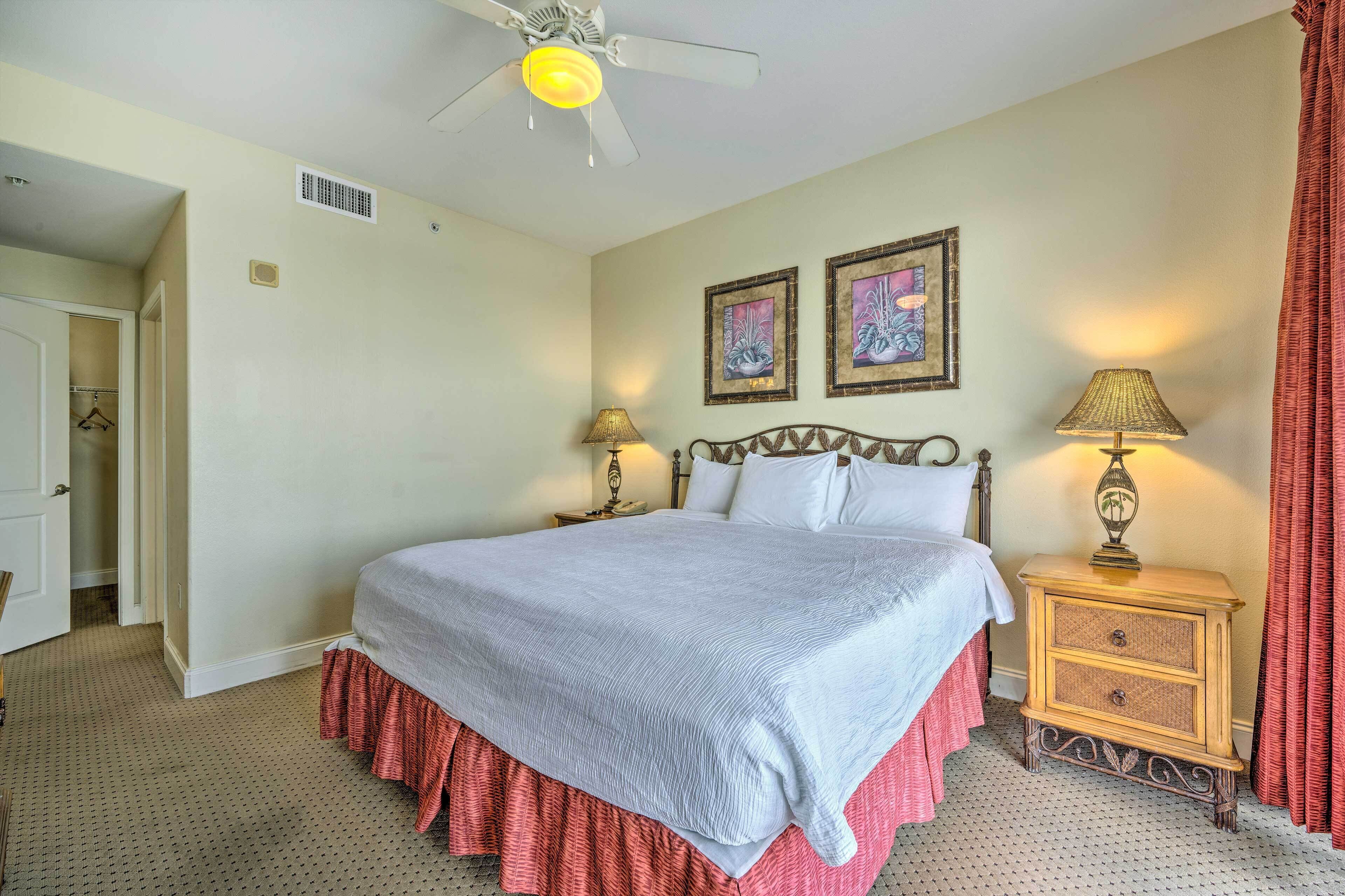 A bedroom with a bed, two bedside lamps, a ceiling fan, and two framed pictures on the wall.