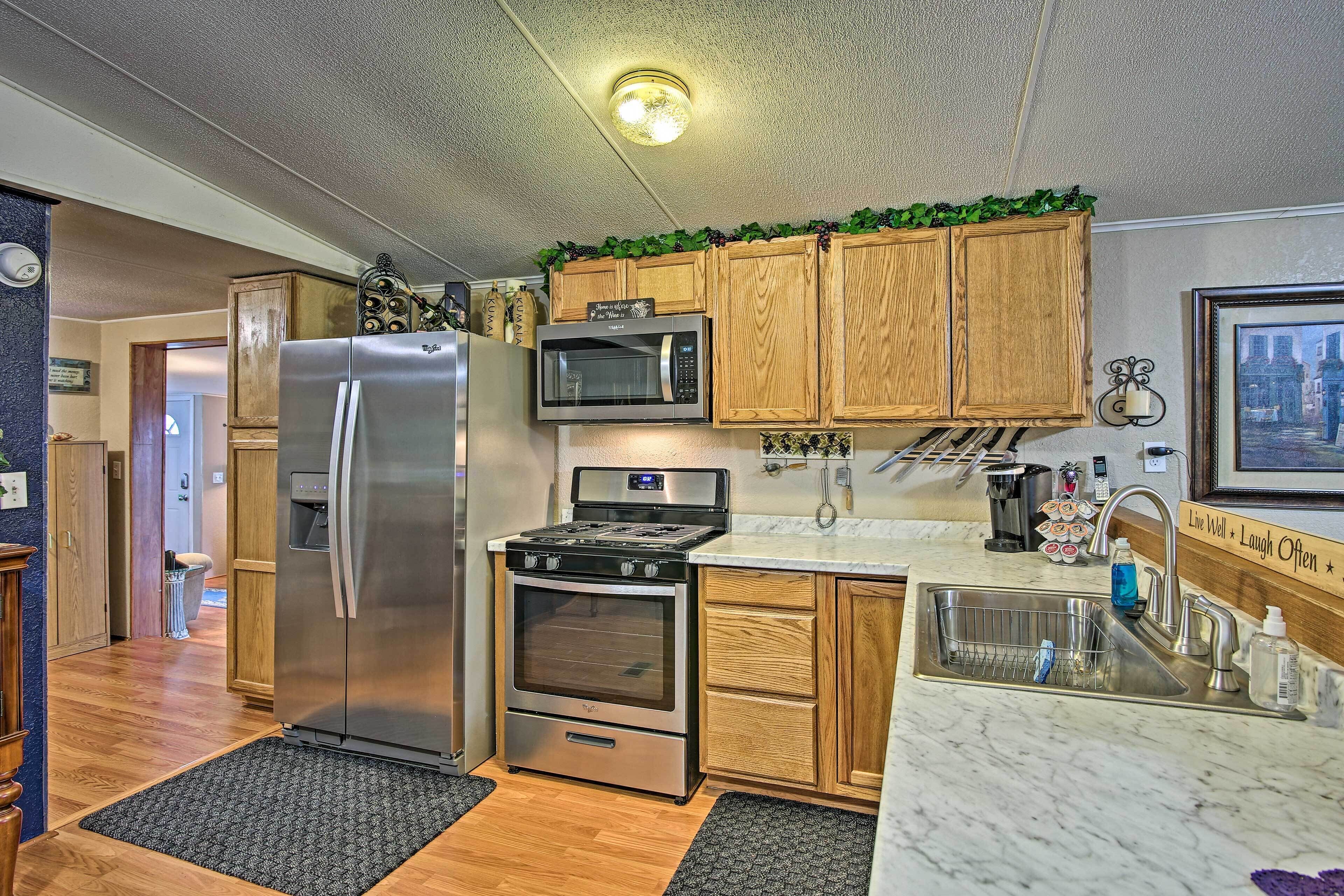 A kitchen with stainless steel appliances, wooden cabinets, a marble countertop, and a sink.