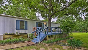 A single-story house with a blue staircase leading to a deck, surrounded by a well-maintained garden and a large tree. - Hot Tub & Deck: Tranquil Home Near Grand Lake (Grove)