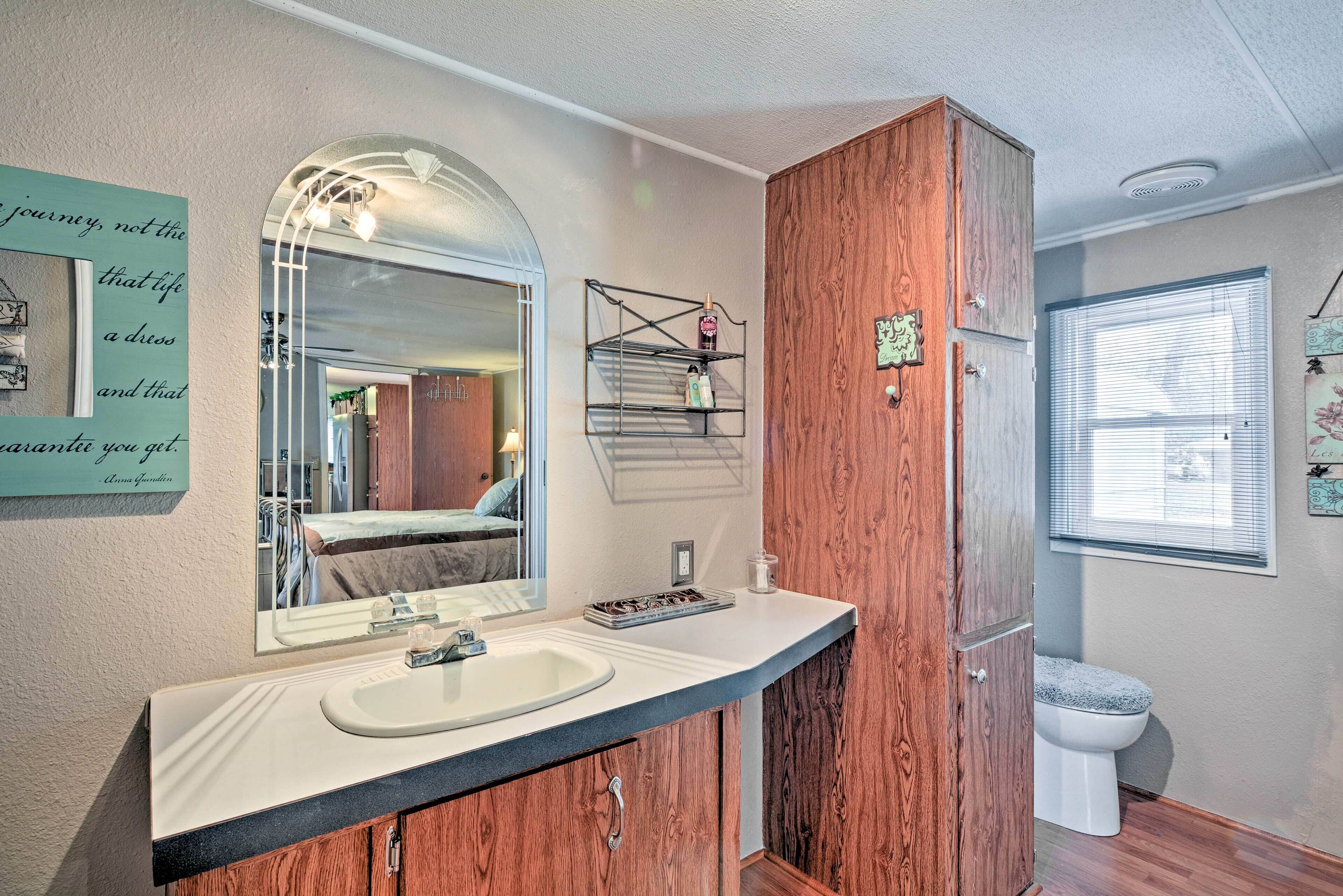 A bathroom with a vanity, mirror, wooden cabinet, and a window with blinds.