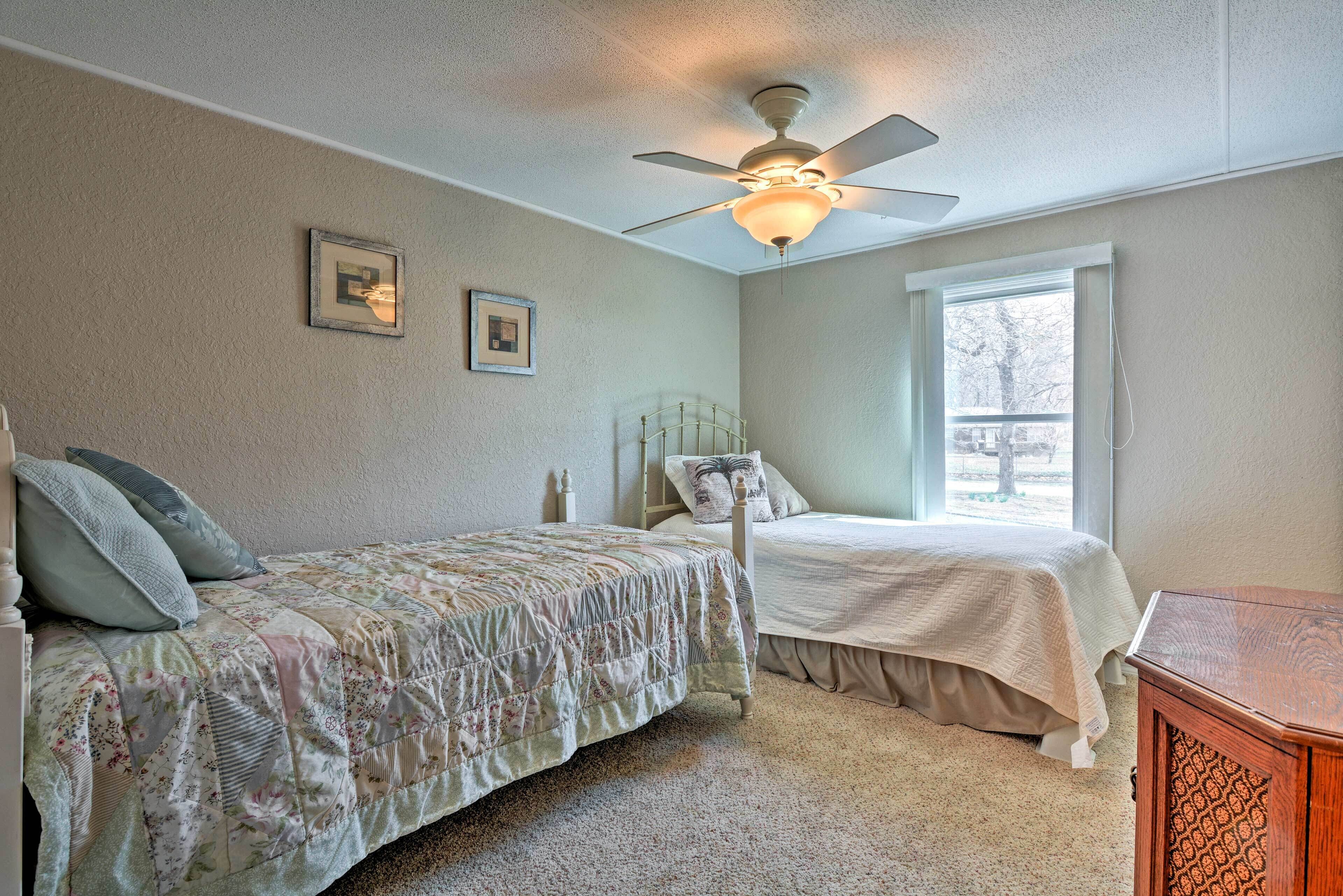 Une chambre avec deux lits, un ventilateur de plafond et une fenêtre donnant sur des arbres.